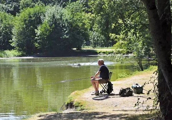 Mężczyzna łowiący ryby w stawie na kempingu Roan Domaine de la Brèche.