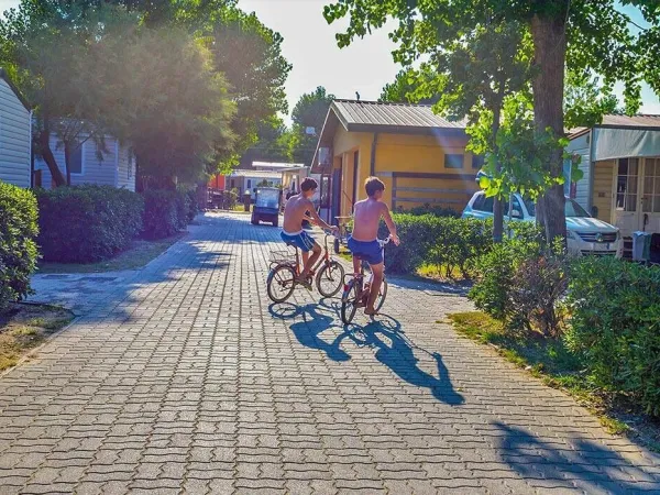 2 młodych chłopców jedzie rowerem przez kemping Roan Sole Family Camping Village.