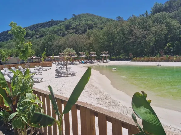 Basen lagunowy z piaszczystą plażą i leżakami na kempingu Roan Verdon Parc.