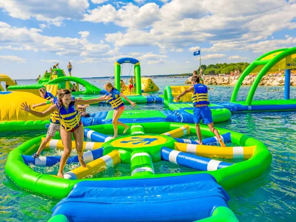 Dzieci bawią się na poduszkach powietrznych w jeziorze na kempingu Roan Le Lac des Vieilles Forges.