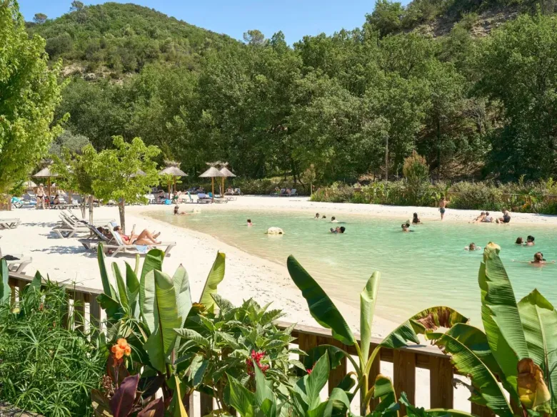 Basen lagunowy z piaszczystą plażą i leżakami na kempingu Roan Verdon Parc.